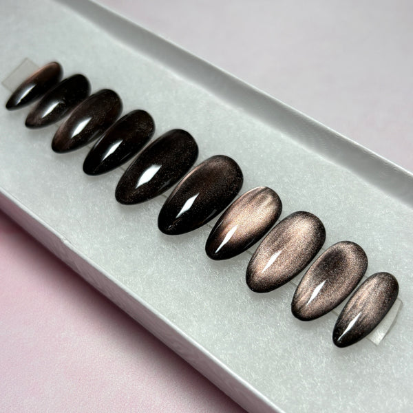 Load image into Gallery viewer, Handmade false nails featuring a dark metallic cat-eye finish that shifts from burnished bronze to deep brown-black, in a short almond shape, displayed in a white presentation box.