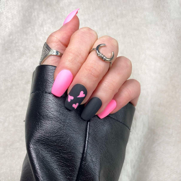 Load image into Gallery viewer, A hand wearing a black leather sleeve showcasing short coffin press-on nails with a pink and black matte design, including pink hearts.