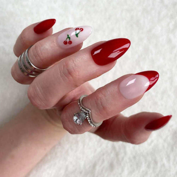 Load image into Gallery viewer, A hand wearing short almond press-on nails in a deep burgundy red with a cherry design on one nail and a French tip on another.