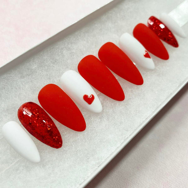 Load image into Gallery viewer, A set of red and white handmade false nails with a heart design and subtle red glitter, in a white presentation box.