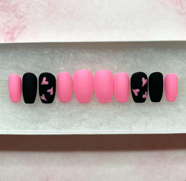 Load image into Gallery viewer, Pink and black press-on nails in a short coffin shape, with a pink heart design on two nails, displayed in a white presentation box.