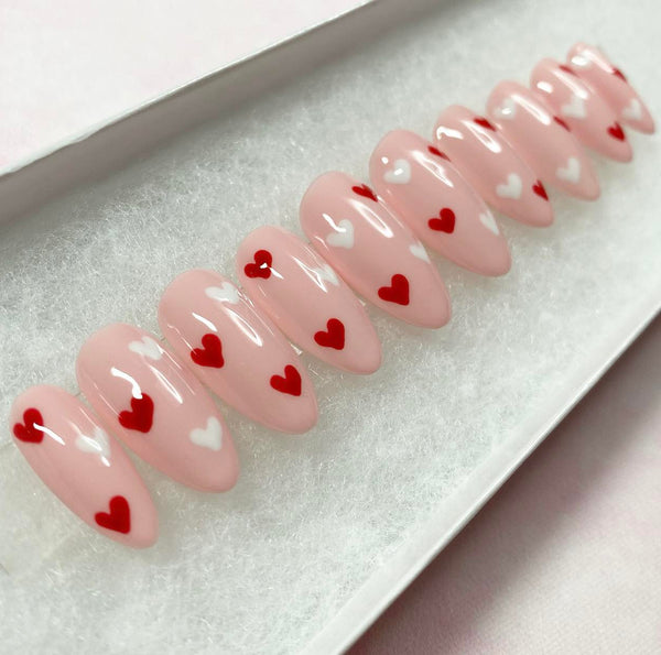 Load image into Gallery viewer, Soft pink almond-shaped press-on nails with red and white heart designs, in a white presentation box.