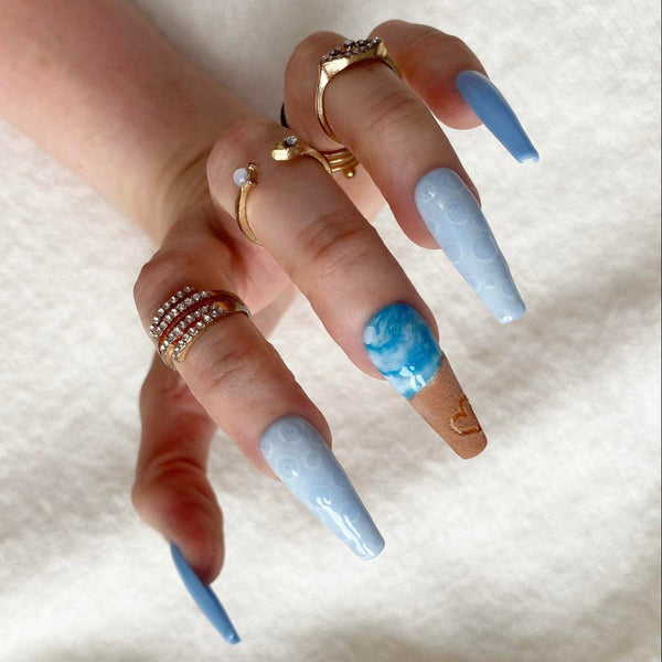 Load image into Gallery viewer, A hand wearing summery press-on nails with a beach themed design featuring a realistic 3D heart drawn in the sand on, and blue-white ocean waves and bubbles, in a long coffin shape, against a soft white background.