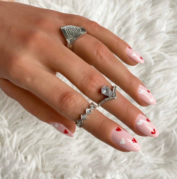 Load image into Gallery viewer, A hand wearing short almond pink press-on nails with red and white heart designs.