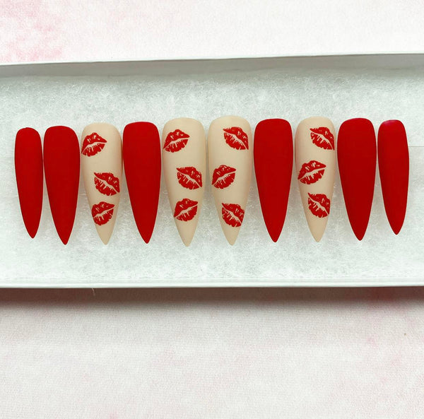 Load image into Gallery viewer, A set of long stiletto press-on nails featuring a mix of matte red and nude nails with a pattern of red lips in a matte finish.