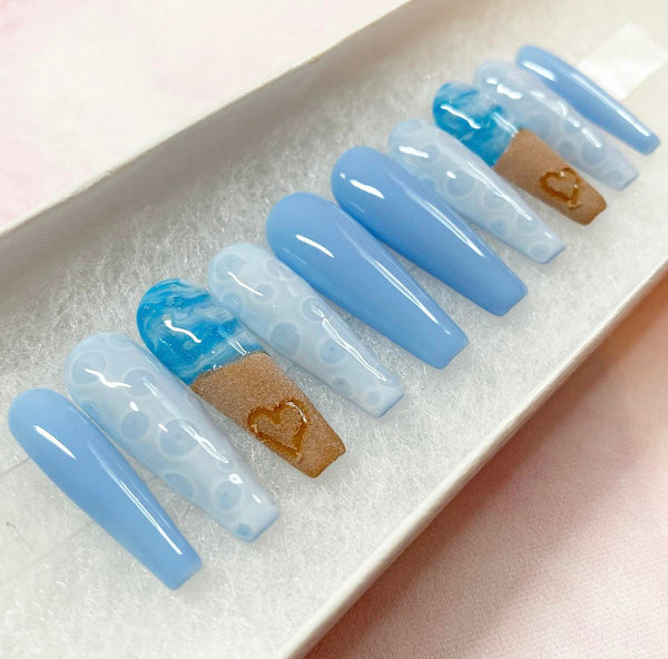 Load image into Gallery viewer, Press-on nails with a summer beach themed design featuring blue-white ocean waves and bubbles, and a realistic heart drawn in sand design, in a long coffin shape, created by Illuminate by Liana.