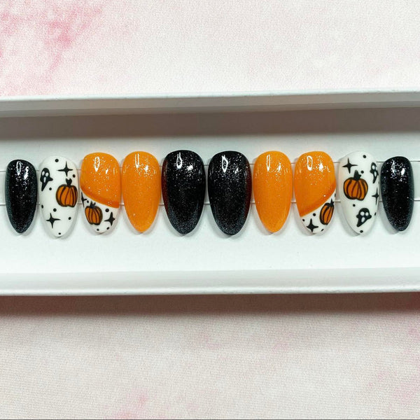Load image into Gallery viewer, Short almond Halloween press-on nails featuring pumpkins, ghosts, and stars designs in orange, black, and white colours, with matte and glossy finishes and subtle glitter, displayed in a white presentation box.