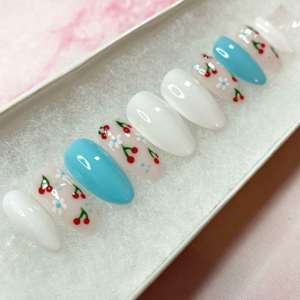 Load image into Gallery viewer, Cherry design press-on nails featuring tiny cherries and floral patterns on a white and blue background, in a short almond shape, displayed in a white presentation box.