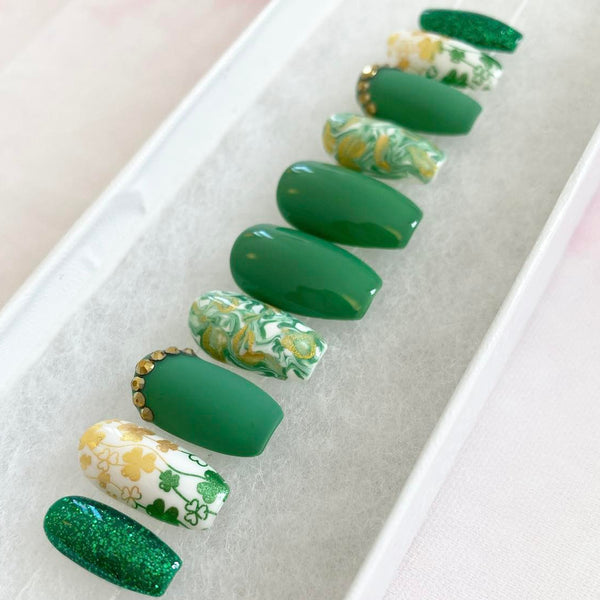 Load image into Gallery viewer, Short coffin St Patrick's Day false nails in green and gold with a shamrock design, gold rhinestones, and a gold-green marble pattern, displayed in a white presentation box.
