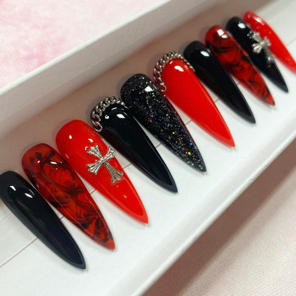 Load image into Gallery viewer, Long stiletto gothic design press-on nails in red and black accented by silver chains and silver cross gems, a marble black-red pattern, and subtle glitter.