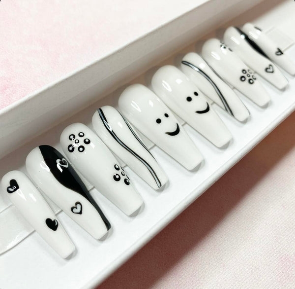 Load image into Gallery viewer, Long coffin press-on nails in black and white featuring various designs including tiny hearts, smiley faces, flowers, and wavy lines, displayed in a white presentation box.