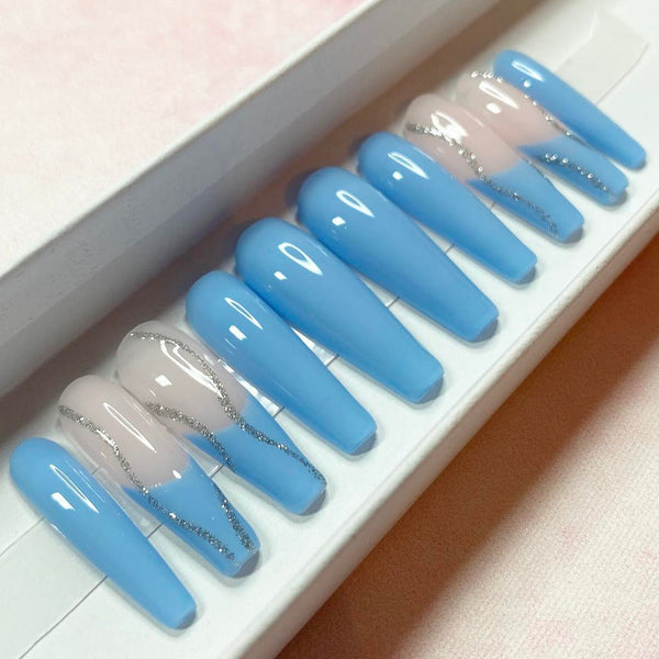 Load image into Gallery viewer, A set of false nails featuring a baby blue colour with a French tip design and silver glitter swirl accents, in a long coffin shape, displayed in a white presentation box.