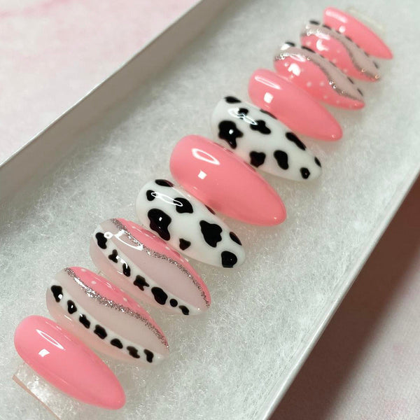 Load image into Gallery viewer, Almond shape handmade press-on nails in pink with a cow print design, in a on a white presentation box.