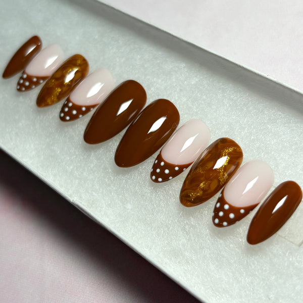 Load image into Gallery viewer, Autumn false nails in a short almond shape, in warm chocolate brown, featuring four solid brown nails, four French tip nails with chocolate-brown tips adorned with white polka dots, and two marble effect brown and metallic gold nails, displayed in a white presentation box.