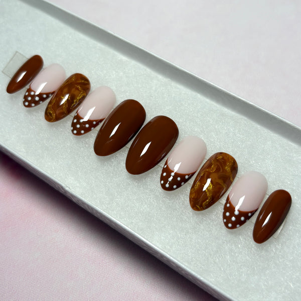 Load image into Gallery viewer, Handmade French tip false nails in a short almond shape, in warm chocolate brown, featuring four solid brown nails, four French tip nails with chocolate-brown tips adorned with white polka dots, and two marble effect brown and metallic gold nails, displayed in a white presentation box.