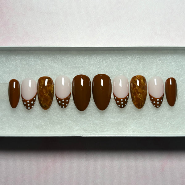 Load image into Gallery viewer, Handmade press-on nails in a short almond shape, in warm chocolate brown, featuring four solid brown nails, four French tip nails with chocolate-brown tips adorned with white polka dots, and two marble effect brown and metallic gold nails, displayed in a white presentation box.