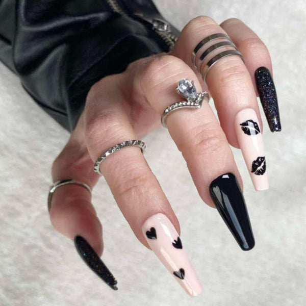 Load image into Gallery viewer, A hand wearing false nails in a long coffin shape, featuring a black and nude design with black hearts and lips, and glitter accents, as well as wearing a black leather-look sleeve and several silver rings.