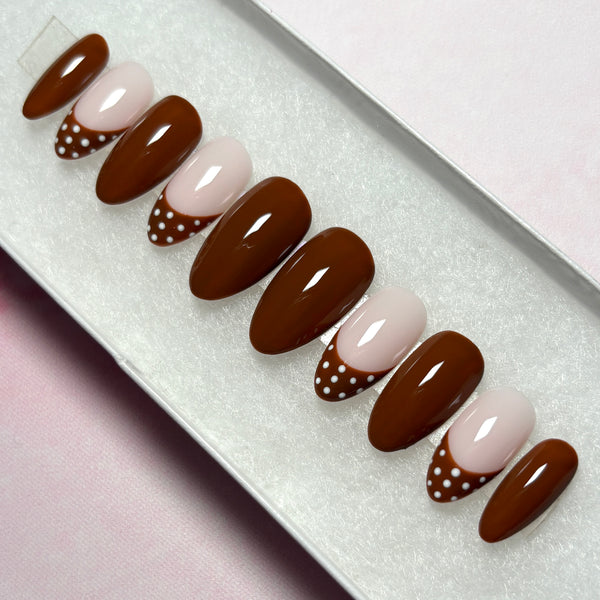 Load image into Gallery viewer, False nails in deep chocolate-brown, featuring four brown French tip nails with white polka dots on the tips, and six glossy brown nails, in a short almond shape, displayed in a white presentation box.