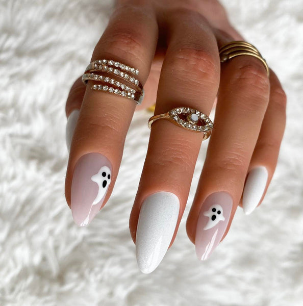 Load image into Gallery viewer, A close-up of a hand with long almond-shaped nails painted in white and pale pink with small black-and-white ghost designs, styled with multiple rings on a white faux-fur background.