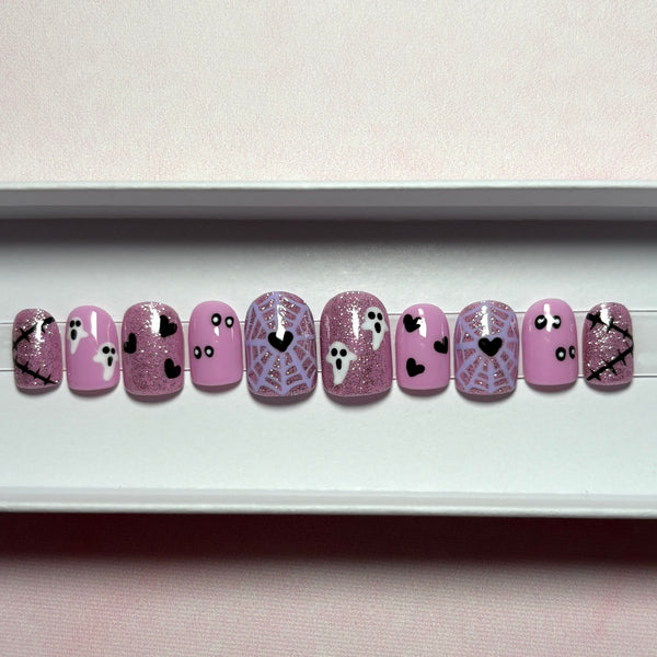 Load image into Gallery viewer, A set of press-on nails with a Halloween theme, featuring pink glitter, lavender spiderwebs, white ghosts, and black hearts, in a short square shape, displayed in a white presentation box.