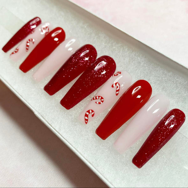 Load image into Gallery viewer, Handmade false nails in a long coffin shape featuring a Christmas design in deep red and pale pink with tiny candy canes on a pale pink base, and deep red glitter, displayed in a white presentation box.