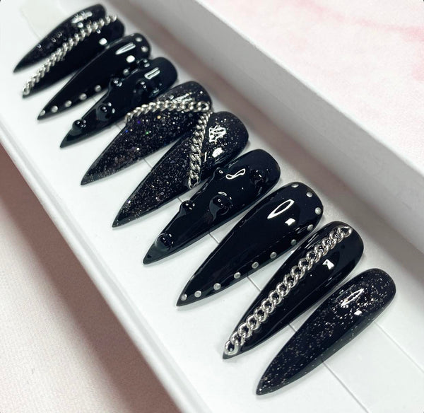 Load image into Gallery viewer, Long stiletto gothic-grunge style false nails in black with black glitter, silver chains, black rhinestones, and a silver chrome stud design, in a white presentation box.