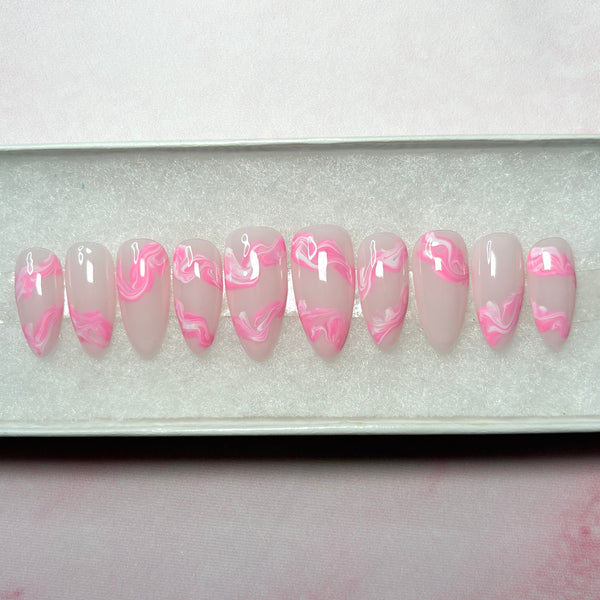 Load image into Gallery viewer, Short almond press-on false nails with a glossy pale pink base and a pink and white marbled swirl pattern near the tips, displayed in a white presentation box