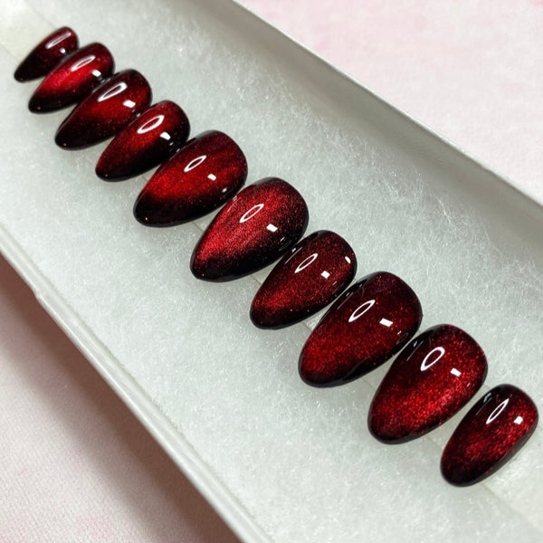 Load image into Gallery viewer, Blood-red cat eye press-on nails that colour-change from red to black, in a short almond shape, displayed in a white presentation box.