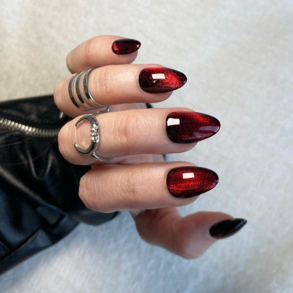 Load image into Gallery viewer, Hand wearing short almond press-on nails in shimmering black-red cat eye gel polish.