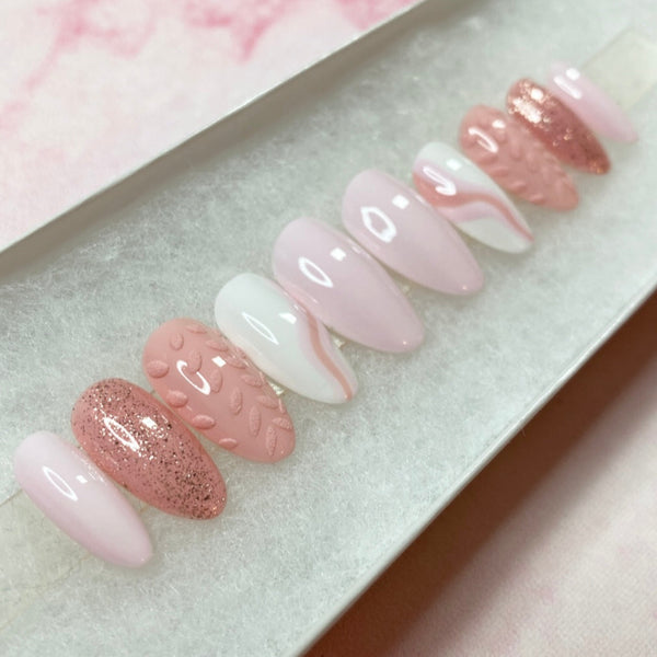 Load image into Gallery viewer, A set of pink stick-on nails in a short almond shape featuring various tones of pink and white, with a 3D leaf design, abstract pink swirls and subtle glitter, displayed in a white presentation box.