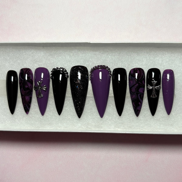 Load image into Gallery viewer, A set of long press-on nails featuring a black and deep purple design with a black-purple marble effect, subtle black and purple glitter, and 3D silver chain and cross embellishments, displayed in a white presentation box.
