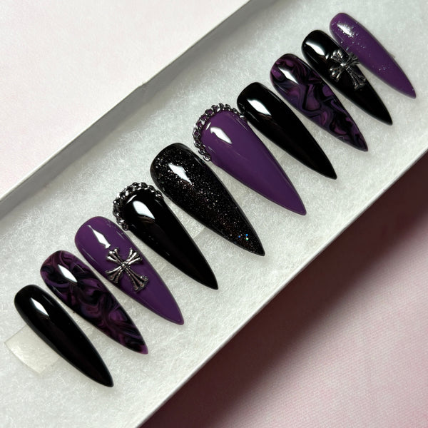Load image into Gallery viewer, A set of stick-on nails in a long stiletto shape, featuring a gothic design in black and deep purple with a black-purple marble effect, subtle black and purple glitter, and 3D silver chain and cross embellishments, displayed in a white presentation box.