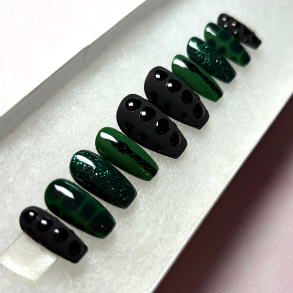 Load image into Gallery viewer, Handmade fake nails in black and dark green, featuring a black snake design on a green background, snake print effect as 3D scales effect as well as subtle green glitter, in a short coffin shape, displayed in a white presentation box.