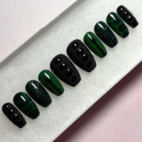 Load image into Gallery viewer, Short coffin glue-on nails with a gothic vibe, in black and deep emerald green, featuring a black snake design on a green background, snake print effect as 3D scales effect as well as subtle green glitter, displayed in a white presentation box.