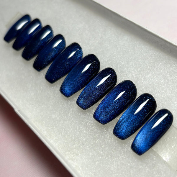 Load image into Gallery viewer, Blue cat-eye handmade stick-on nails that colour-shift from a shimmery dark blue through black, handmade in a short coffin shape, displayed in a white presentation box.