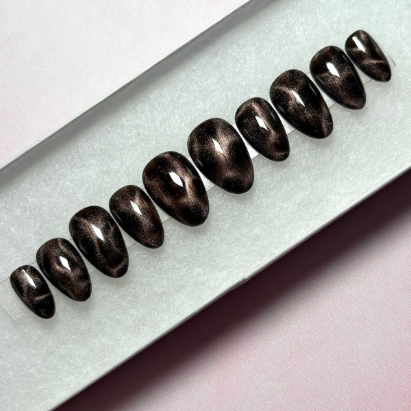 Load image into Gallery viewer, A set of dark metallic press-on nails with a shimmering bronze-brown magnetic cat-eye finish, displayed in a white presentation box.