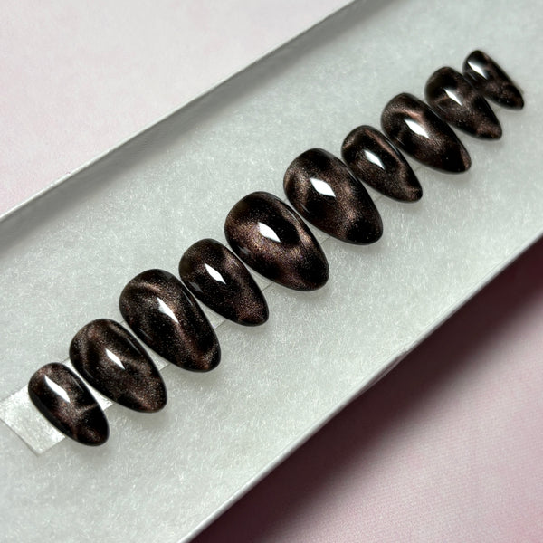Load image into Gallery viewer, Short almond stick-on nails in black and bronze brown cat eye that shimmers and glitters, giving a leopard print or tortoise shell effect, displayed in a white presentation box.