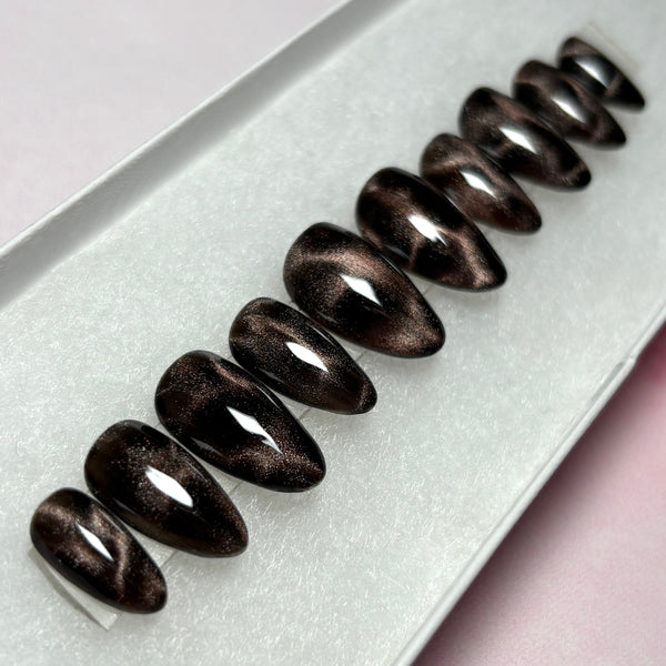 Load image into Gallery viewer, A set of false nails in black and bronze brown cat eye that shimmers and glitters, giving a leopard print or tortoise shell effect, in a short almond shape, displayed in a white presentation box.