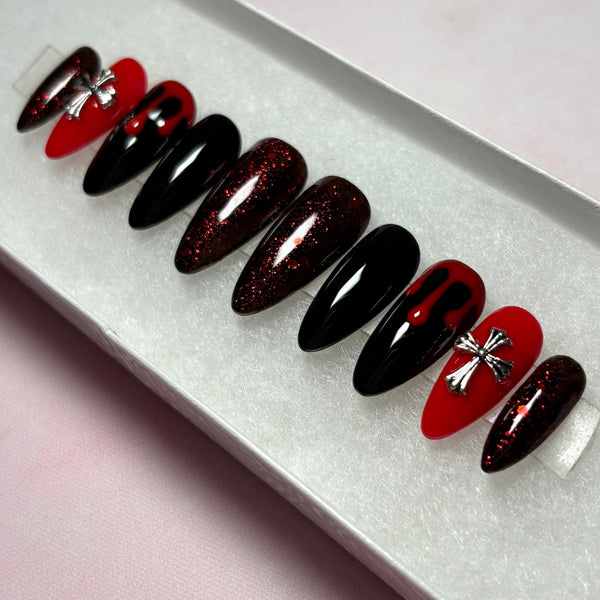 Load image into Gallery viewer, Gothic goth grunge false nails in red and black featuring deep red blood drips on two black nails, 3D metallic silver cross gems on two red nails, deep red glitter on four nails, and two solid black nails, in a long almond shape, displayed in a white presentation box.