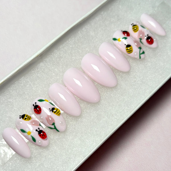 Load image into Gallery viewer, Summer-Spring press-on nails in pale pink featuring 3D ladybirds, bees and flowers, in a short almond shape, displayed in a white presentation box.