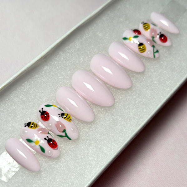 Load image into Gallery viewer, Spring press-on nails in pastel pink with 3D ladybirds, bees and flowers artwork, in a short almond shape, displayed in a white presentation box.