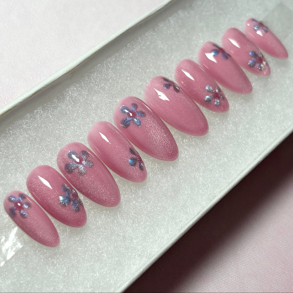 Load image into Gallery viewer, Pink spring-summer press-on nails in a shimmery cat eye blush pink, with a lilac cat-eye flower on each nail, in a short almond shape, in a white presentation box.
