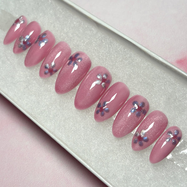 Load image into Gallery viewer, Short almond shape false nails in a shimmery cat eye blush pink, each nail adorned with a lilac cat-eye flower, presented in a pretty white box.