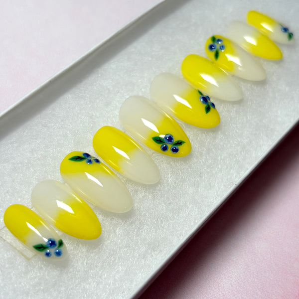 Load image into Gallery viewer, Press-on nails in a lemon-yellow ombre featuring delicate 3D blueberries designed on several nails, in a short almond shape, displayed in a white presentation box.