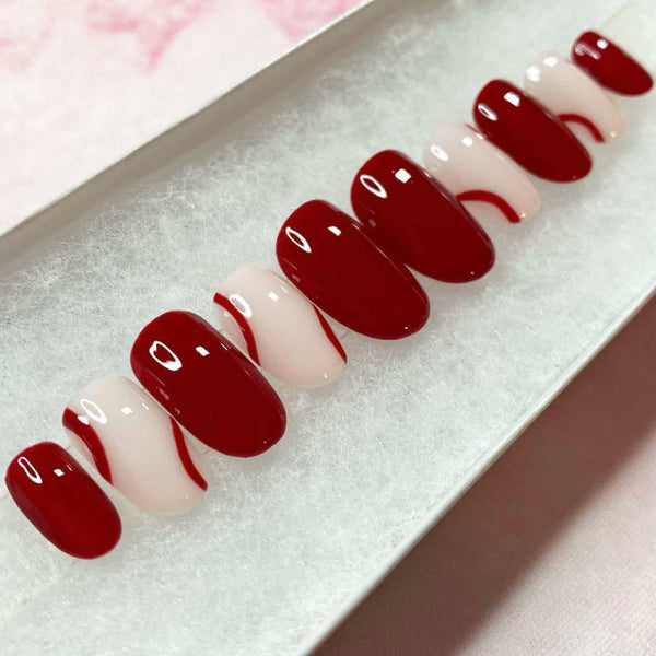 Load image into Gallery viewer, Short round false nails painted in a deep burgundy red color with natural tips and burgundy lines, in a white presentation box.