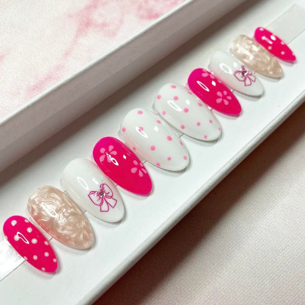 Load image into Gallery viewer, Press-on nails featuring a Barbiecore design with alternating pink and white nails, some with floral patterns, polka dots, bows, and gemstones, in a short almond shape.