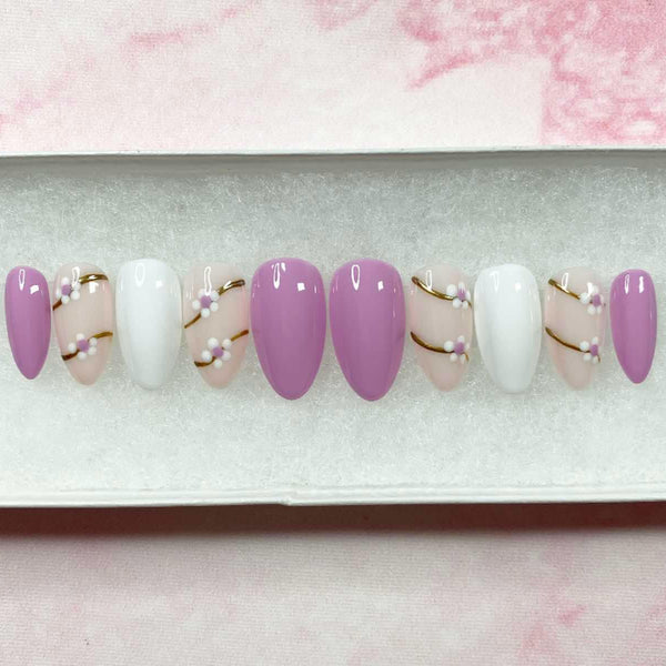 Load image into Gallery viewer, Handmade short almond spring-summer design press-on nails displayed in a gradient of pink, white, and lilac with floral designs on gold chrome branches.