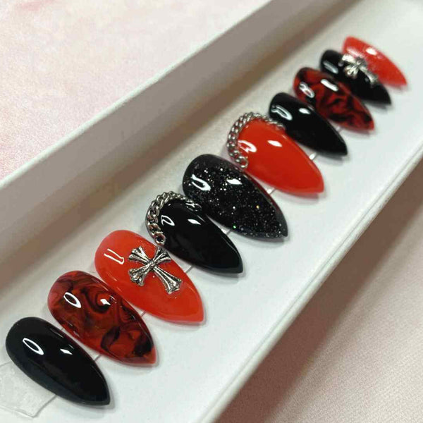 Load image into Gallery viewer, Short stiletto press-on nails in a red and black gothic style accented by silver chains along the bottom of two nails, silver crosses, a marble black-red pattern, and subtle glitter.