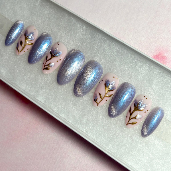 Load image into Gallery viewer, Handmade press-on nails in a spring-summer design of shimmering lilac-silver cat eye and a delicate floral design with gold chrome stems and leaves, and shimmering lilac petals on a soft pink base.