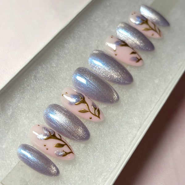 Load image into Gallery viewer, Spring-summer design fake nails with shimmering lilac-silver cat eye and delicate flowers with gold chrome stems and leaves, and glittery lilac petals on a soft pink base, from Illuminate by Liana